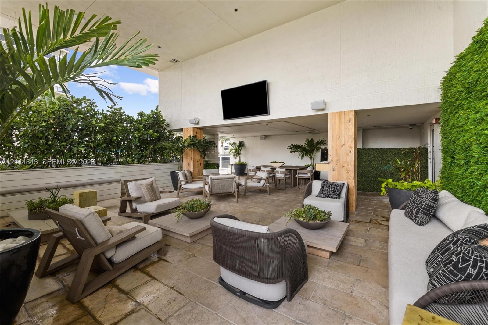 Covered outdoor terrace featuring natural stone tile flooring, structural wooden columns, a mounted television, and integrated vertical greenery