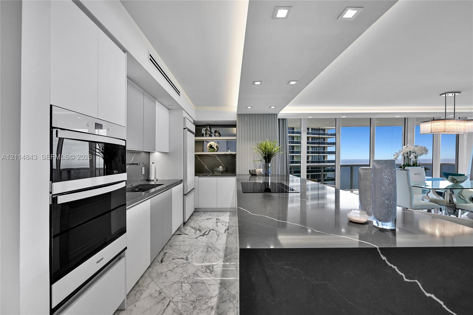 Kitchen featuring high-gloss cabinetry, stone-finish countertops, integrated double wall ovens, recessed ceiling lighting, and floor-to-ceiling windows