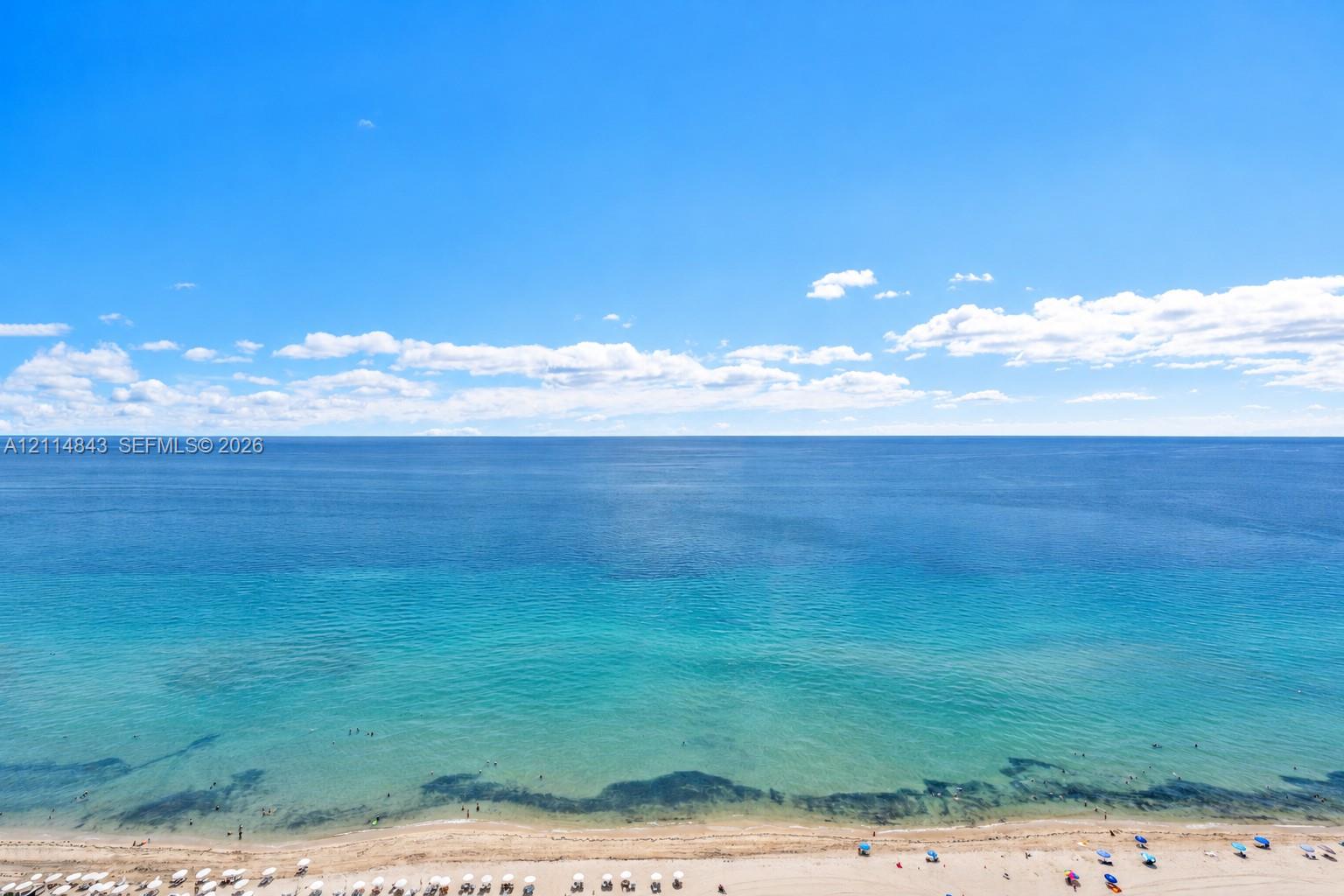 Panoramic oceanfront perspective featuring clear blue waters, expansive horizon, and sandy shoreline