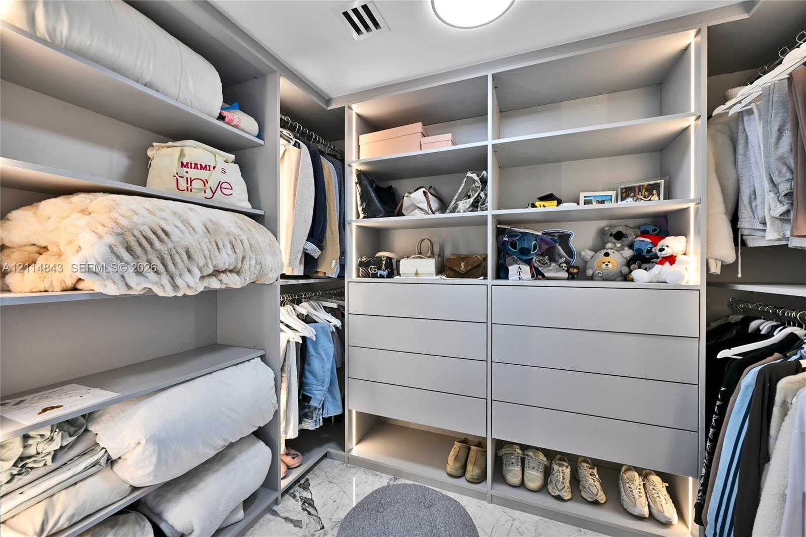 Walk-in closet featuring custom built-in cabinetry with integrated LED lighting, tiered shelving, multiple storage drawers, and floor-to-ceiling organization systems