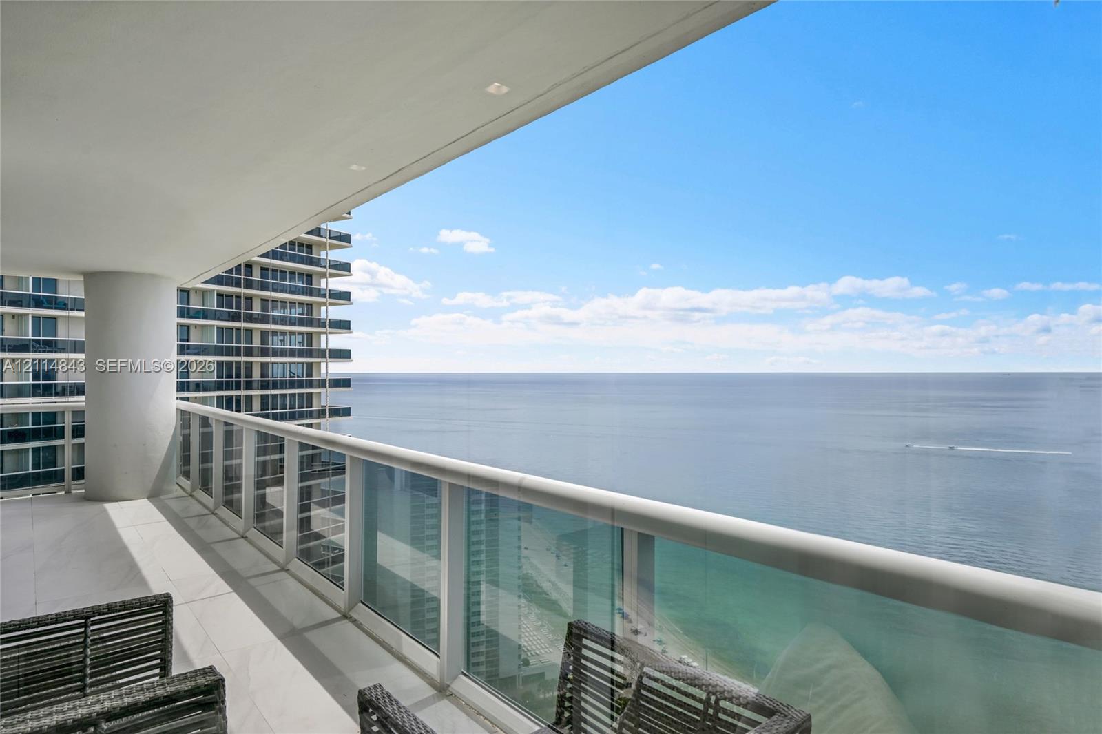 Covered private terrace featuring large-format tile flooring, glass panel railings, and recessed ceiling lighting with ocean scenery