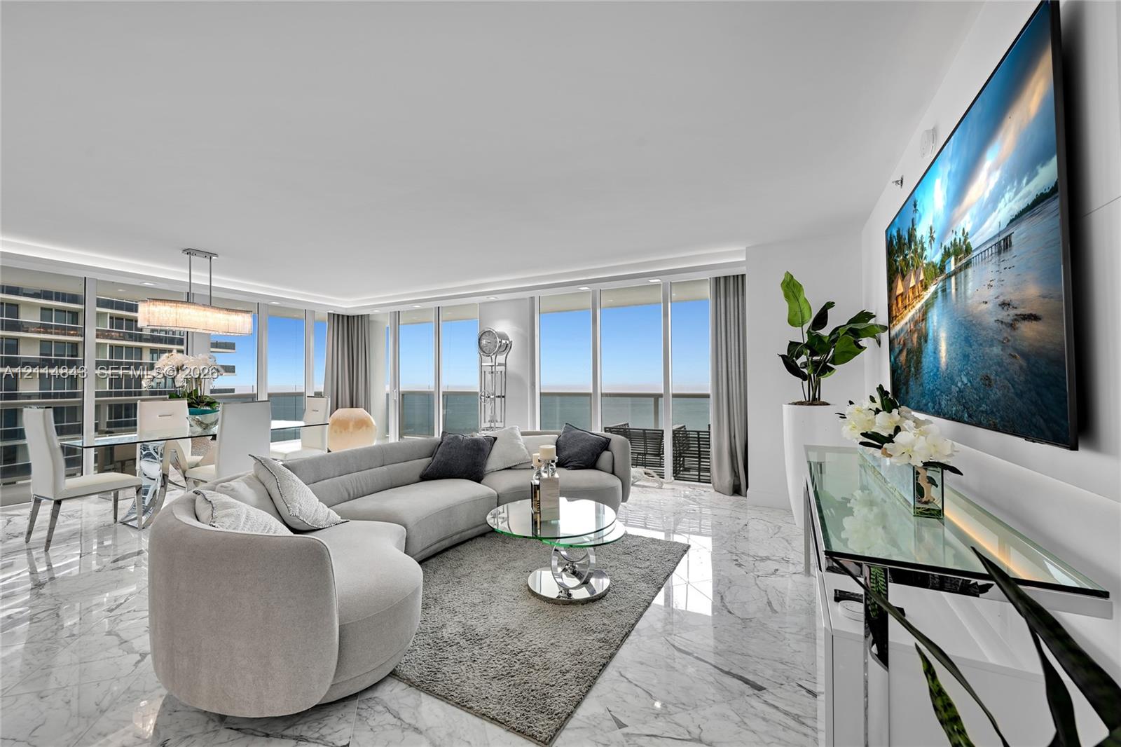 Open-concept living space featuring floor-to-ceiling windows, polished stone flooring, recessed lighting, and a multi-tiered crystal chandelier