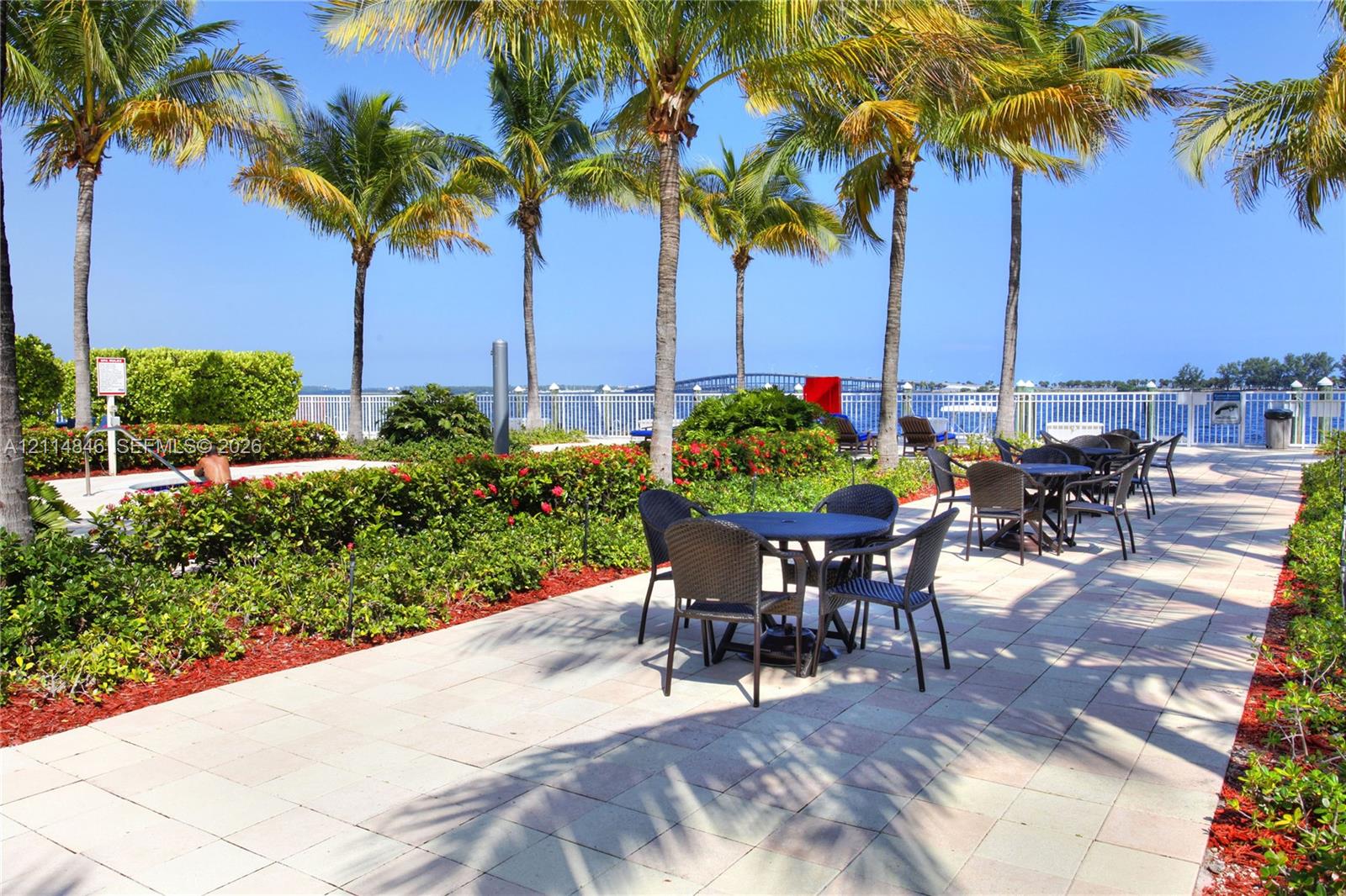 Waterfront patio featuring stone paver flooring, manicured landscaping, and mature palm trees