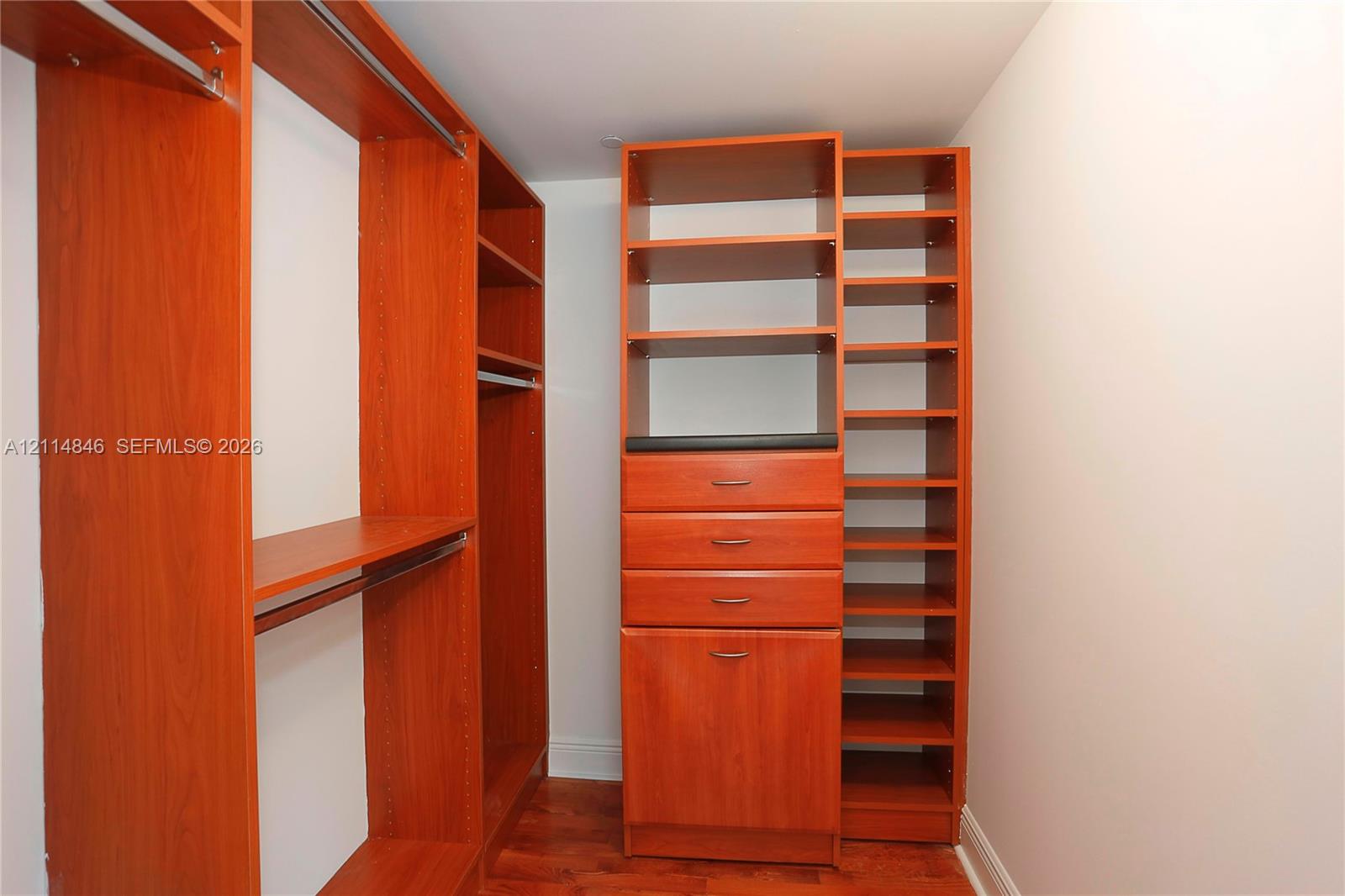 Custom closet featuring wood-finish cabinetry, integrated shelving, multiple storage drawers with metal hardware, and wood-finish flooring