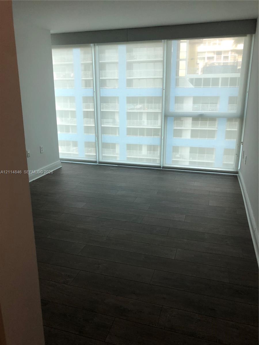 Floor-to-ceiling windows with roller shades and dark wood-finish flooring