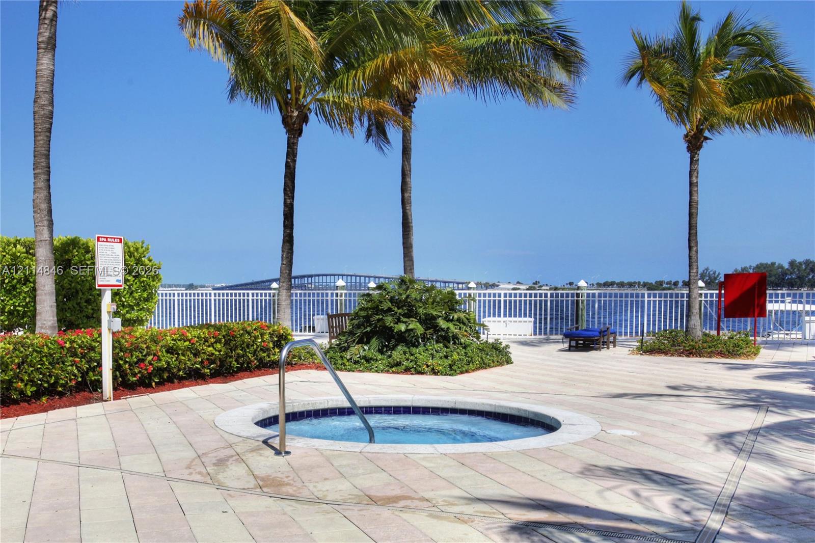 In-ground spa with stone-paver surround, metal safety railing, and mature palm trees