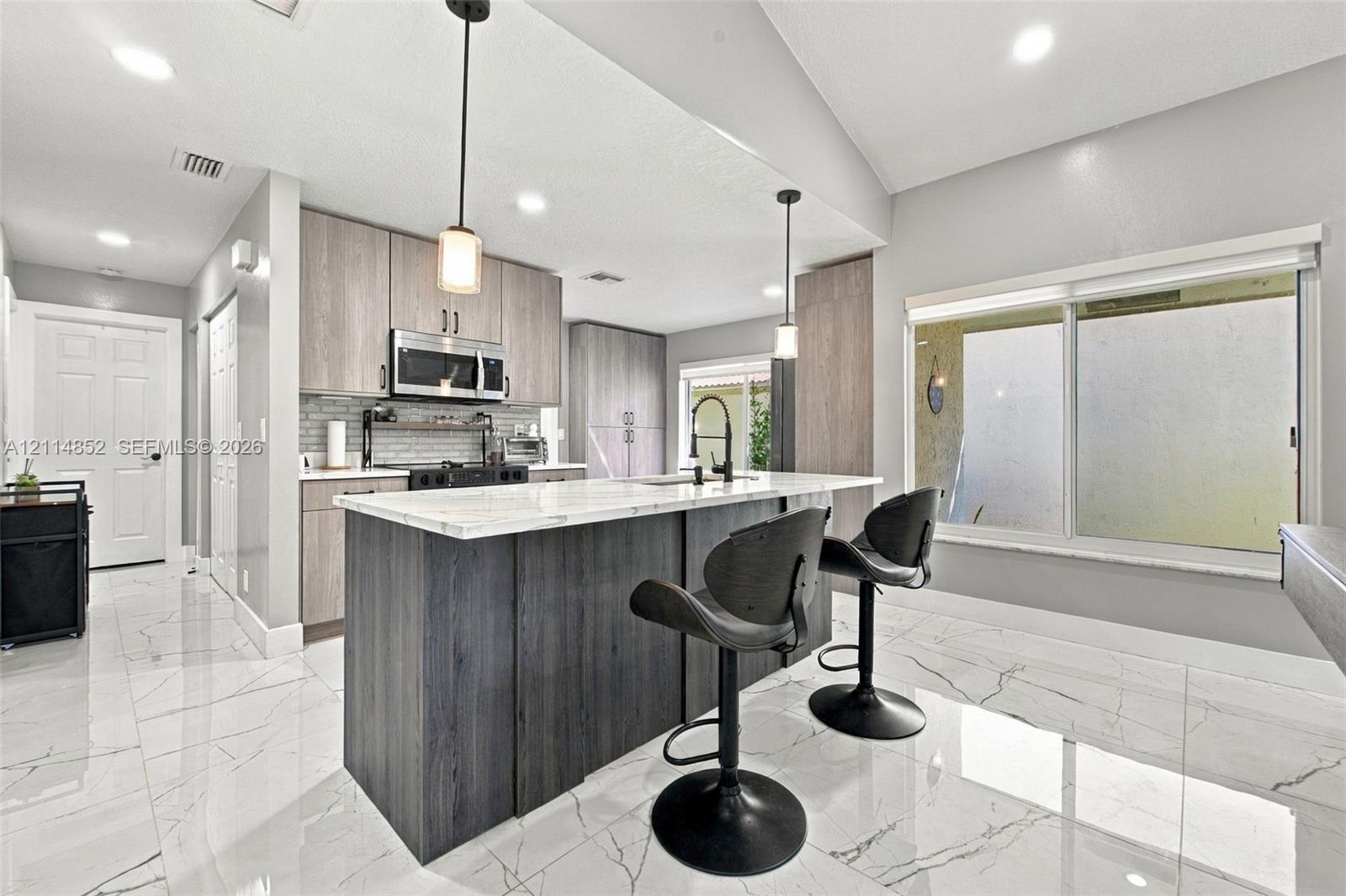 Kitchen featuring wood-finish cabinetry, a central island with a stone-top surface, large-format tile flooring, recessed lighting, and dual pendant light fixtures