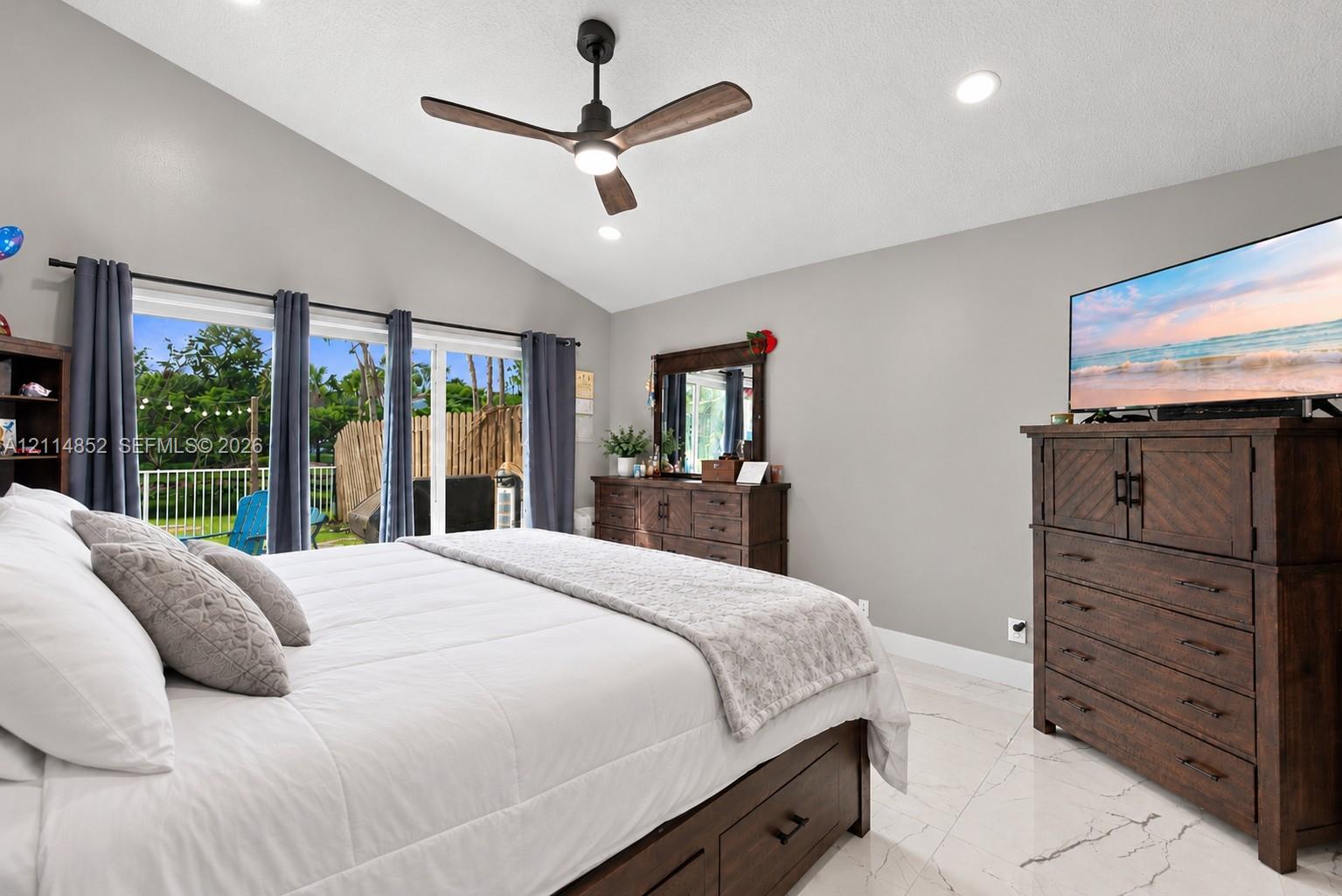 Vaulted ceiling with a matte black modern ceiling fan, large glass sliding doors, and polished stone-finish flooring