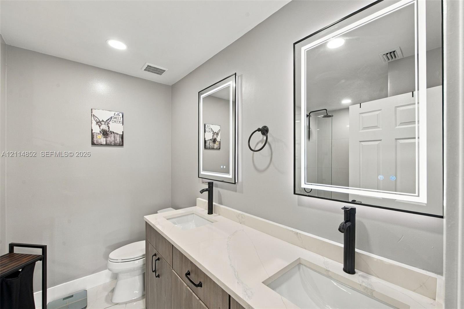 Double vanity featuring a light-toned countertop, dual rectangular undermount sinks, matte black tall-spout faucets, and rectangular backlit mirrors