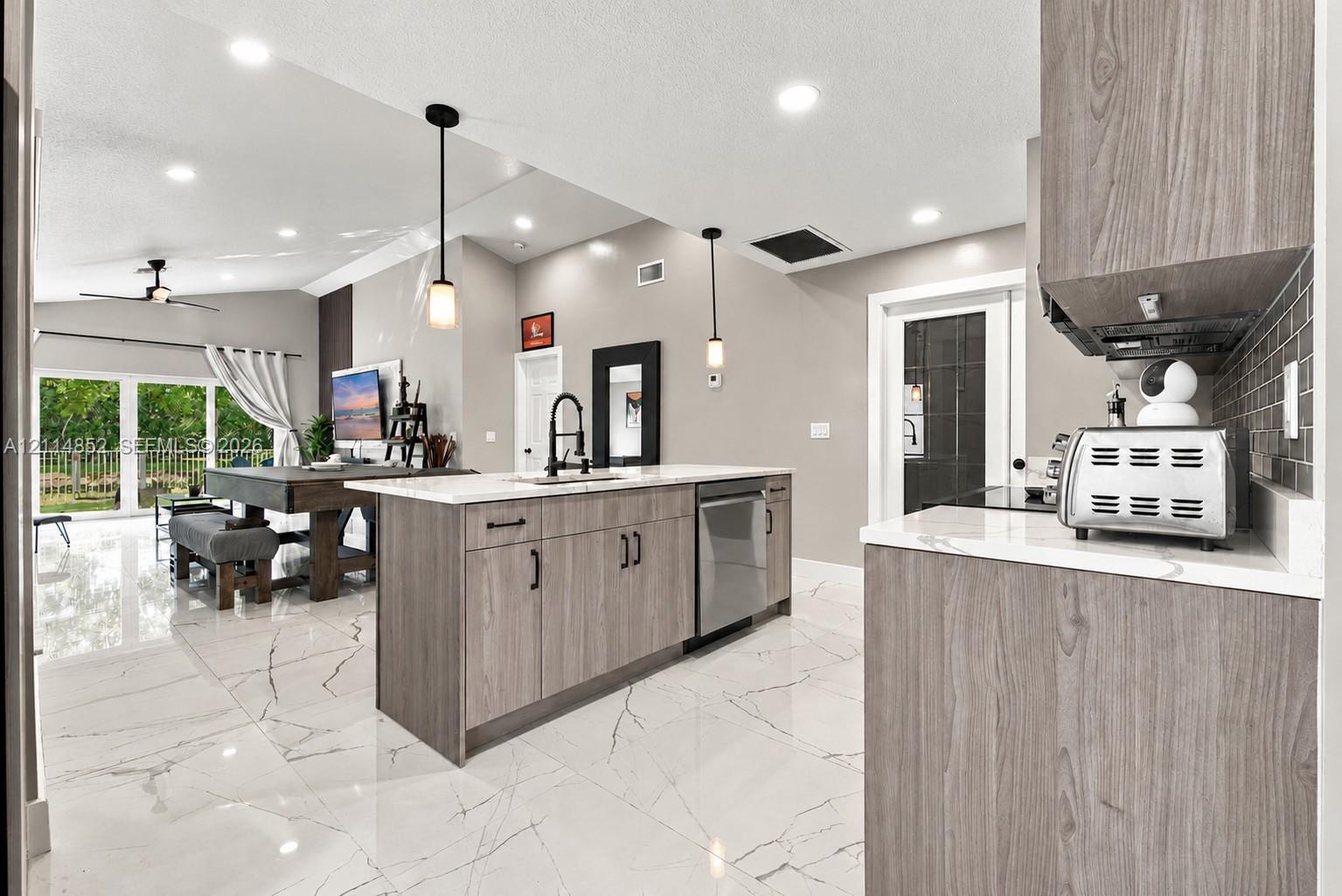 Kitchen featuring wood-finish cabinetry, stone-style countertops, recessed ceiling lighting, pendant light fixtures, and large-format tile flooring