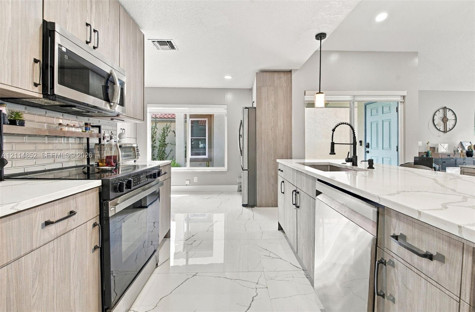 Kitchen featuring wood-finish cabinetry, stone-surface countertops with waterfall edge, large-format tile flooring, stainless steel appliances, and a matte black gooseneck faucet