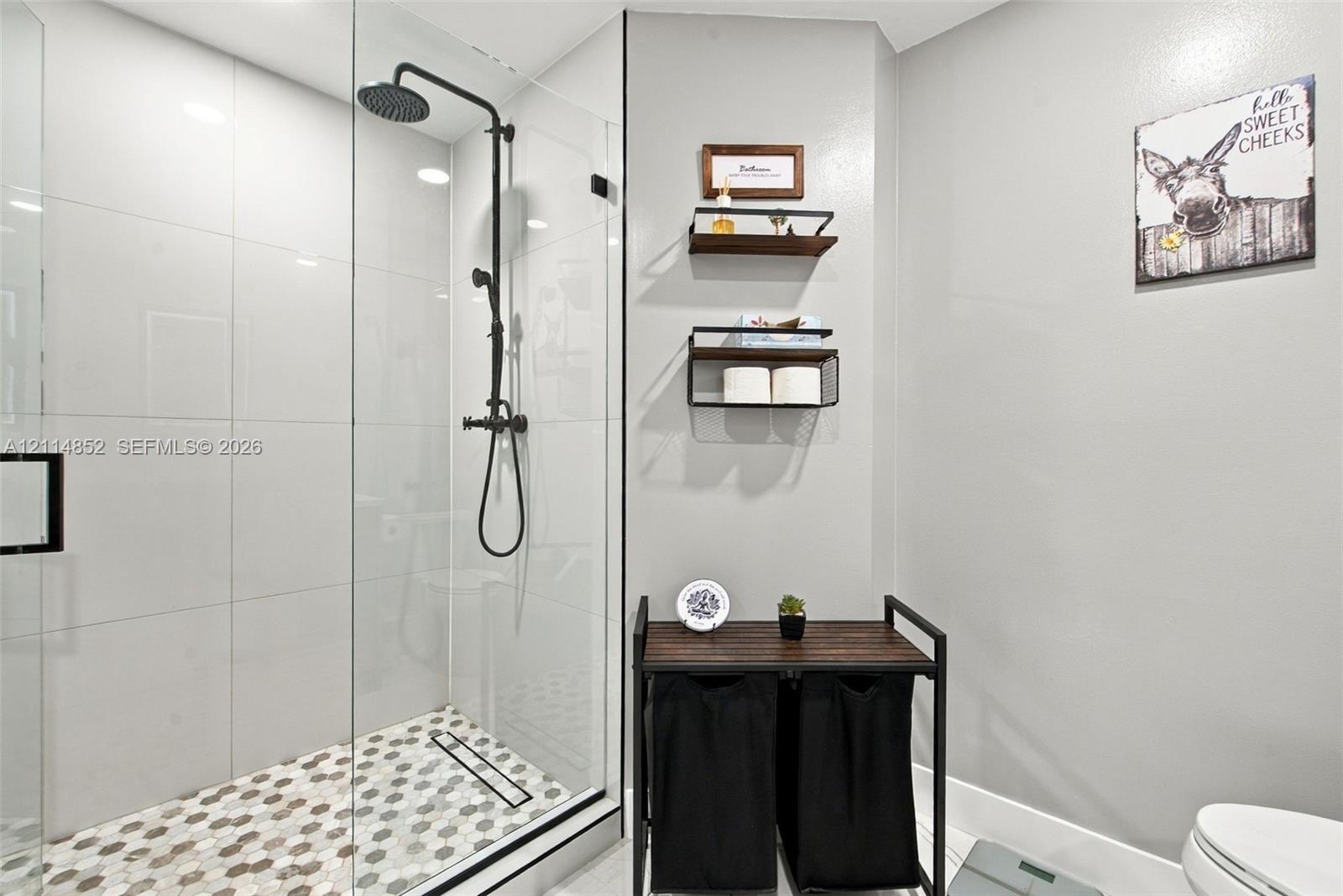 Walk-in shower featuring a frameless glass enclosure, matte black rainfall showerhead, and hexagonal mosaic floor tile