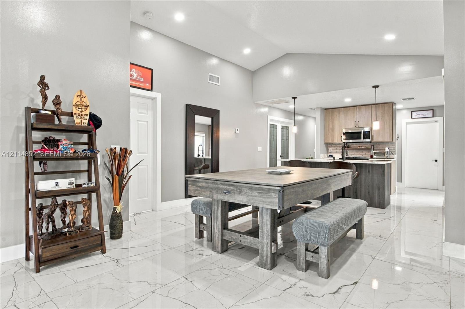 Open-concept interior featuring vaulted ceilings, polished tile flooring with marble-style veining, recessed lighting, and a kitchen equipped with two-tone cabinetry and stainless-steel appliances