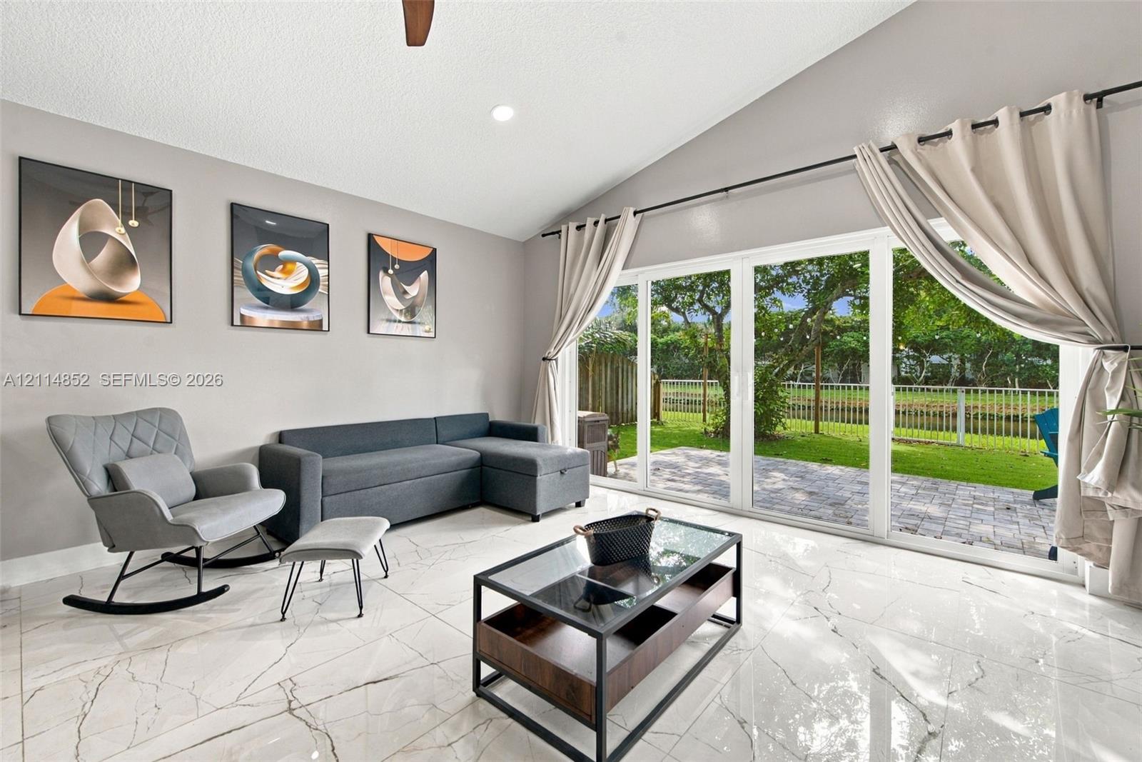 Vaulted ceiling, polished stone-finish flooring, and expansive glass sliding doors providing entry to the outdoor patio
