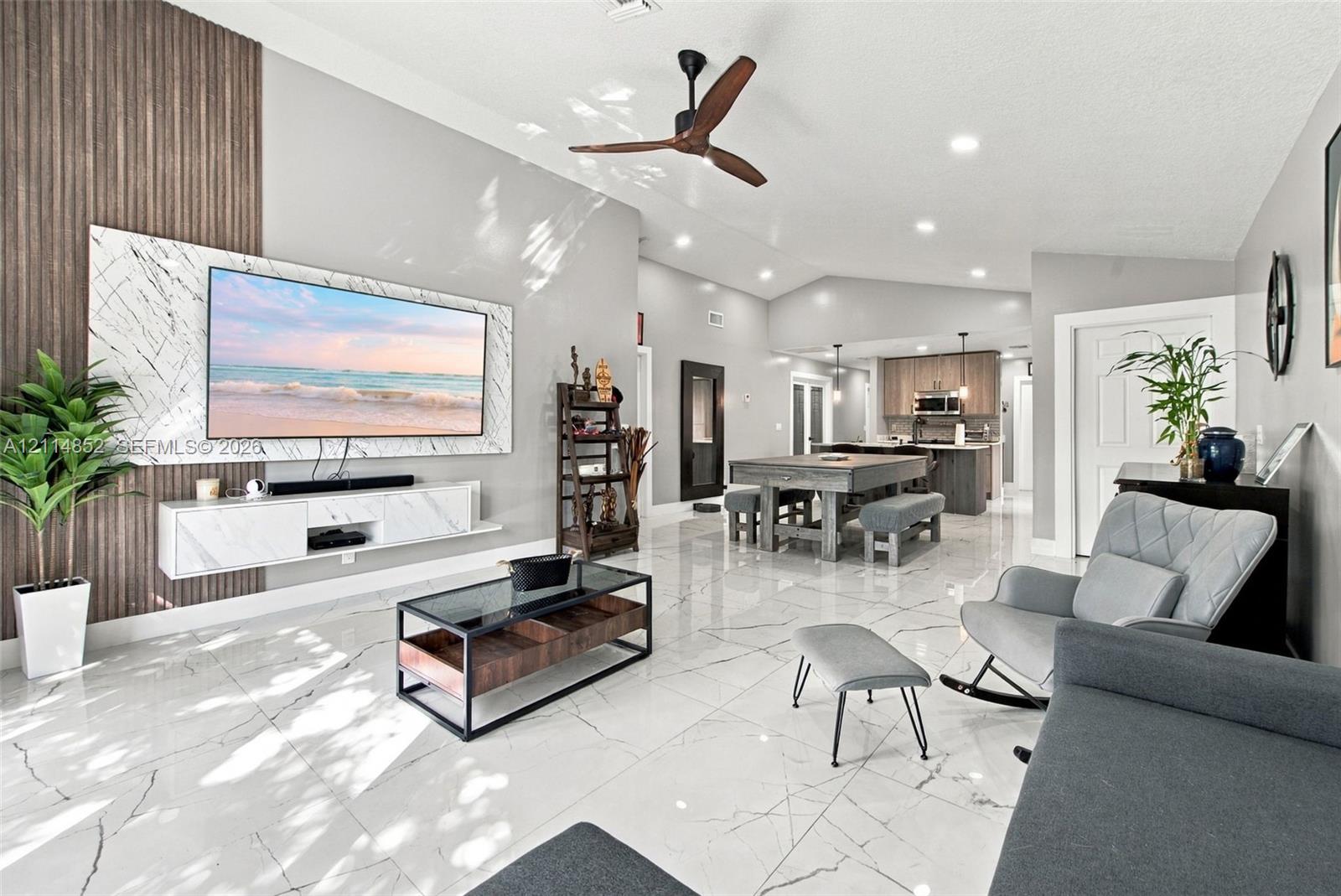 Open-concept living space featuring high vaulted ceilings, large-format polished tile flooring, a vertical wood-slat accent wall, and a custom wall-mounted floating media console with stone-finish cladding