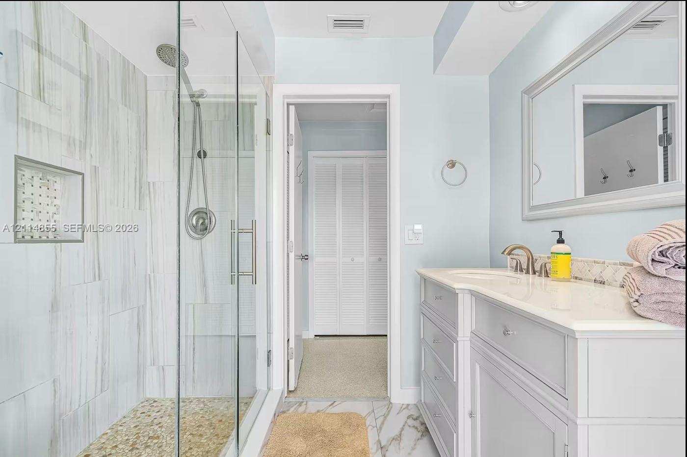 Walk-in glass-enclosed shower with a rainfall showerhead, integrated tiled wall niche, pebble stone flooring, stone-finish wall tile, and a single-sink vanity with a light-toned countertop