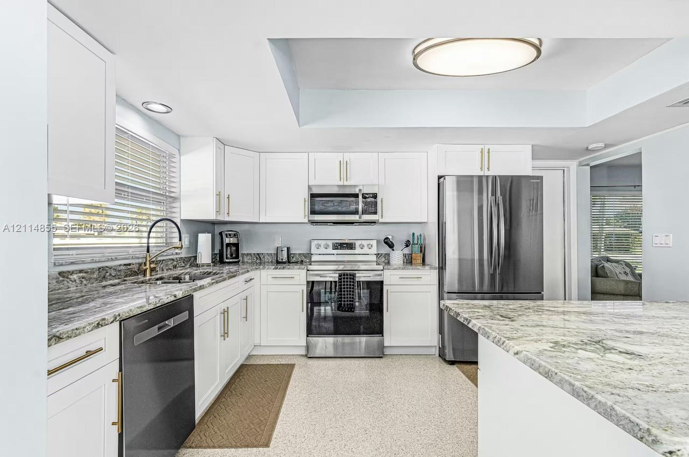 Kitchen featuring white cabinetry, stone countertops, stainless steel appliances, a high-arc faucet, and recessed ceiling lighting