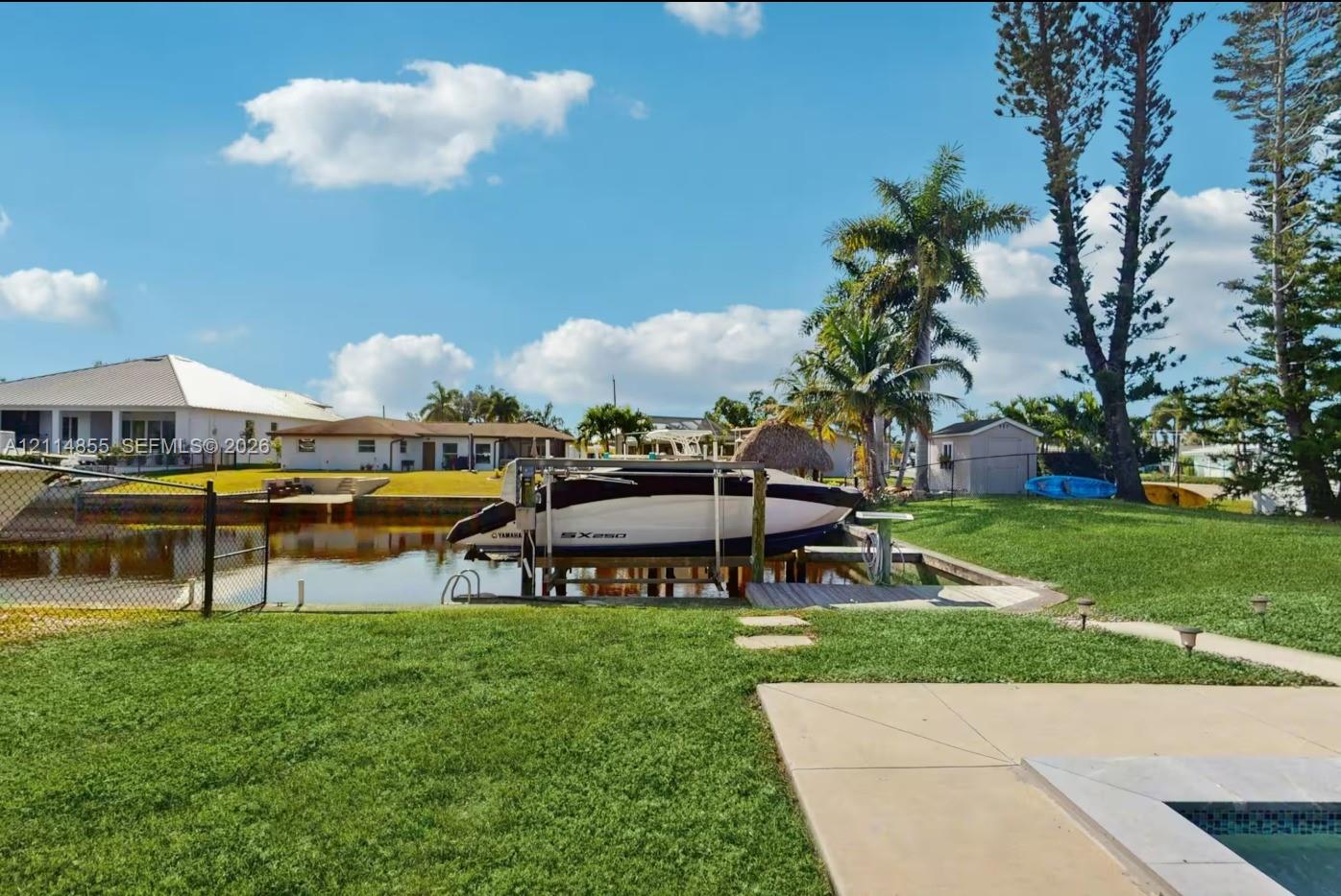 Waterfront backyard featuring a private boat lift, a canal bulkhead, an expansive lawn, and a concrete patio