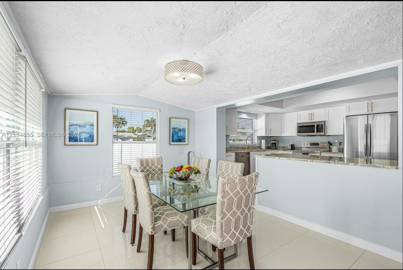 Dining area featuring large-format tile flooring, a semi-flush mount drum light fixture, and windows with horizontal blinds