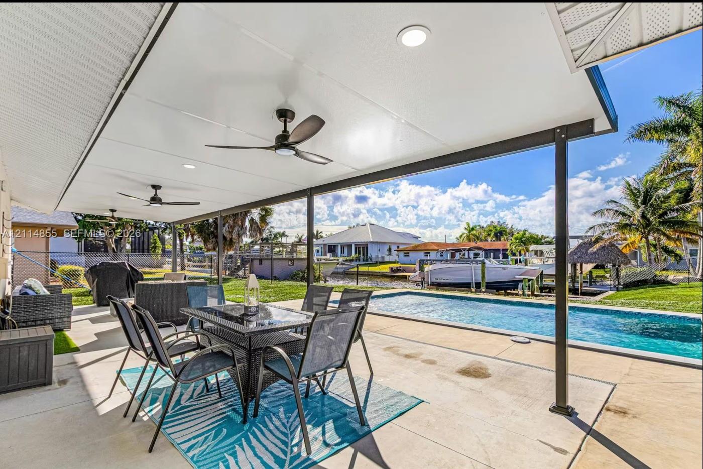 Covered outdoor patio featuring a concrete floor, recessed ceiling lighting, and two ceiling fans, overlooking an in-ground swimming pool and canal frontage