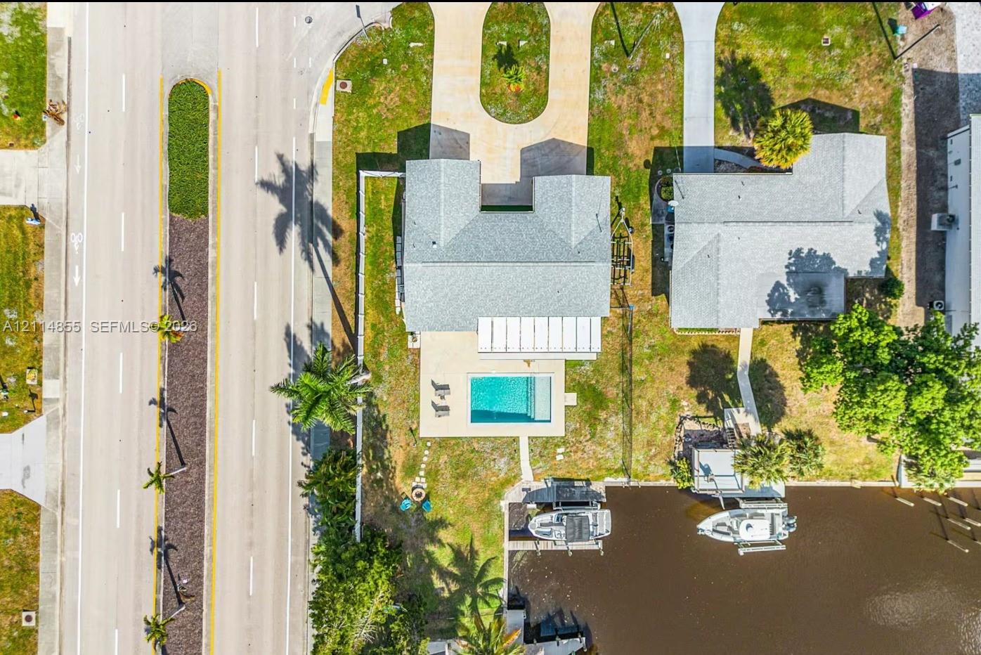 Aerial perspective featuring a waterfront property with a private swimming pool, paved driveway, and dedicated boat slip