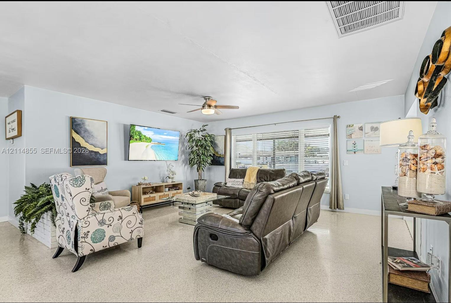 Living area featuring large format terrazzo flooring, multi-pane window with horizontal blinds, and ceiling-mounted fan with integrated light fixture