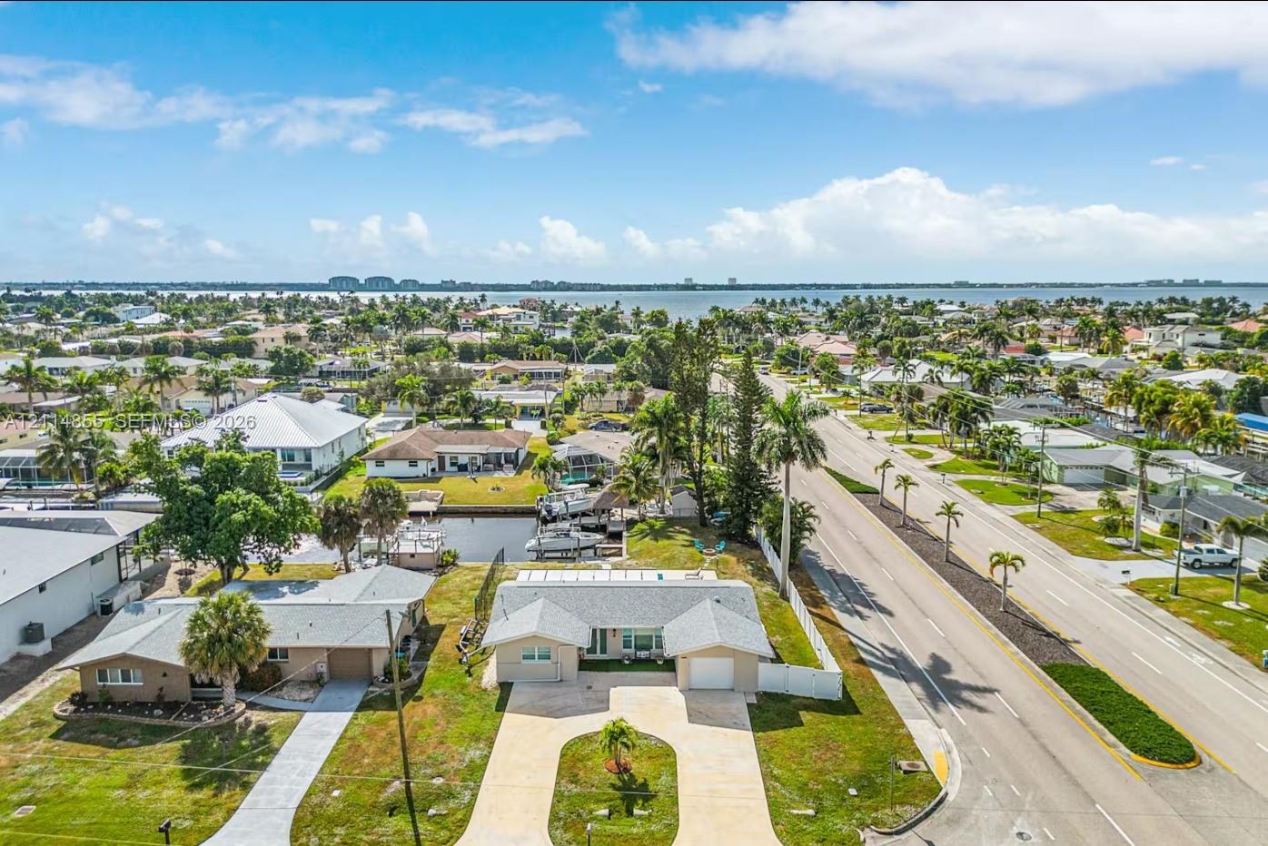 Aerial perspective featuring a single-story residence with a concrete driveway, attached garage, private canal access with boat dock, and surrounding tropical landscaping