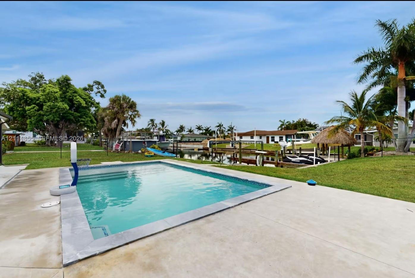In-ground swimming pool with concrete decking, private dock, and mature palm trees situated on a waterfront lot