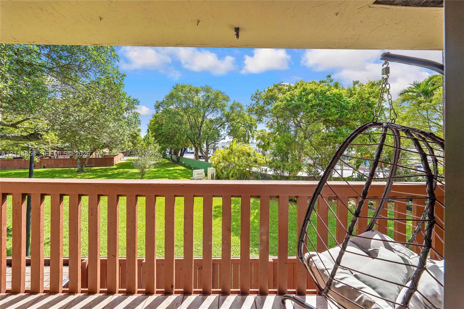 Covered balcony featuring a wood-style railing and an outdoor space overlooking a landscaped yard with mature trees