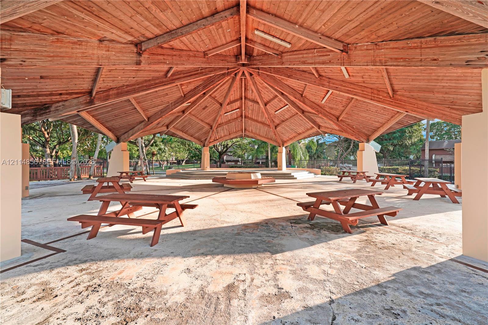 Covered outdoor pavilion featuring a vaulted wood-beam ceiling, concrete flooring, and raised central platform