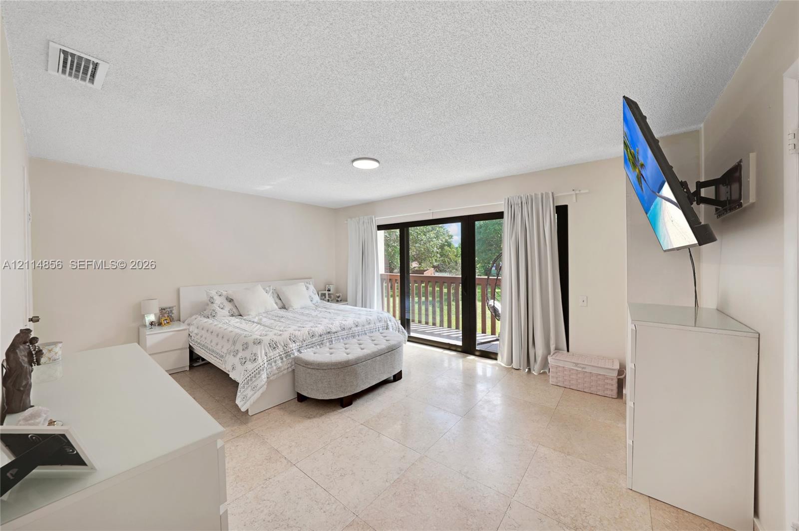 Neutral-toned room featuring large-format tile flooring, sliding glass doors, and a balcony with wood-finish railings