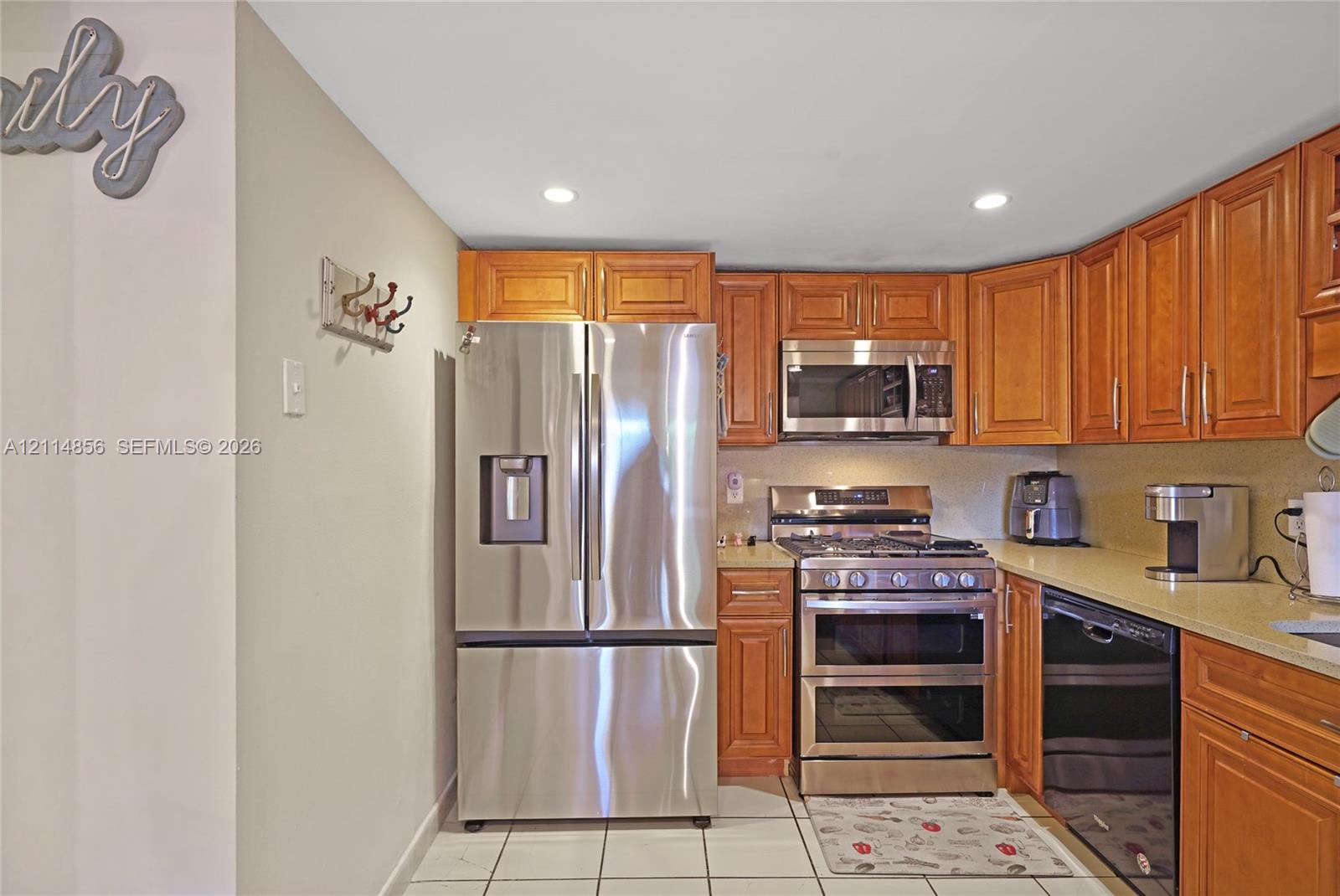 Kitchen featuring natural wood cabinetry, stainless steel appliances, solid surface countertops, recessed lighting, and tile flooring Kitchen featuring natural wood cabinetry, stainless steel appliances, solid surface countertops, recessed lighting, and tile flooring