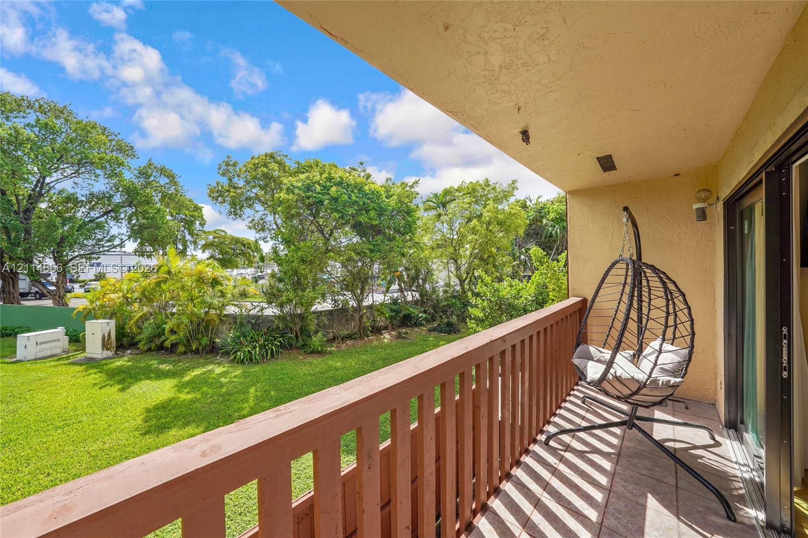 Covered balcony featuring wood-style railings, tile flooring, and direct access to a green space with mature landscaping