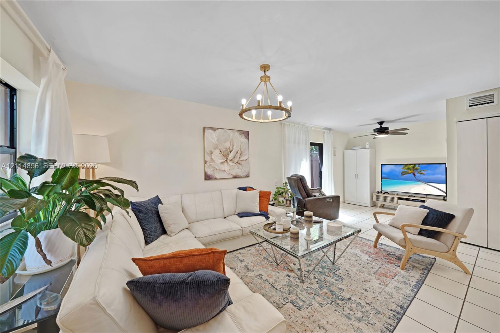 Neutral-toned interior space featuring light-colored tile flooring, a circular chandelier with brass finish, and a ceiling-mounted fan with light fixture Neutral-toned interior space featuring light-colored tile flooring, a circular chandelier with brass finish, and a ceiling-mounted fan with light fixture