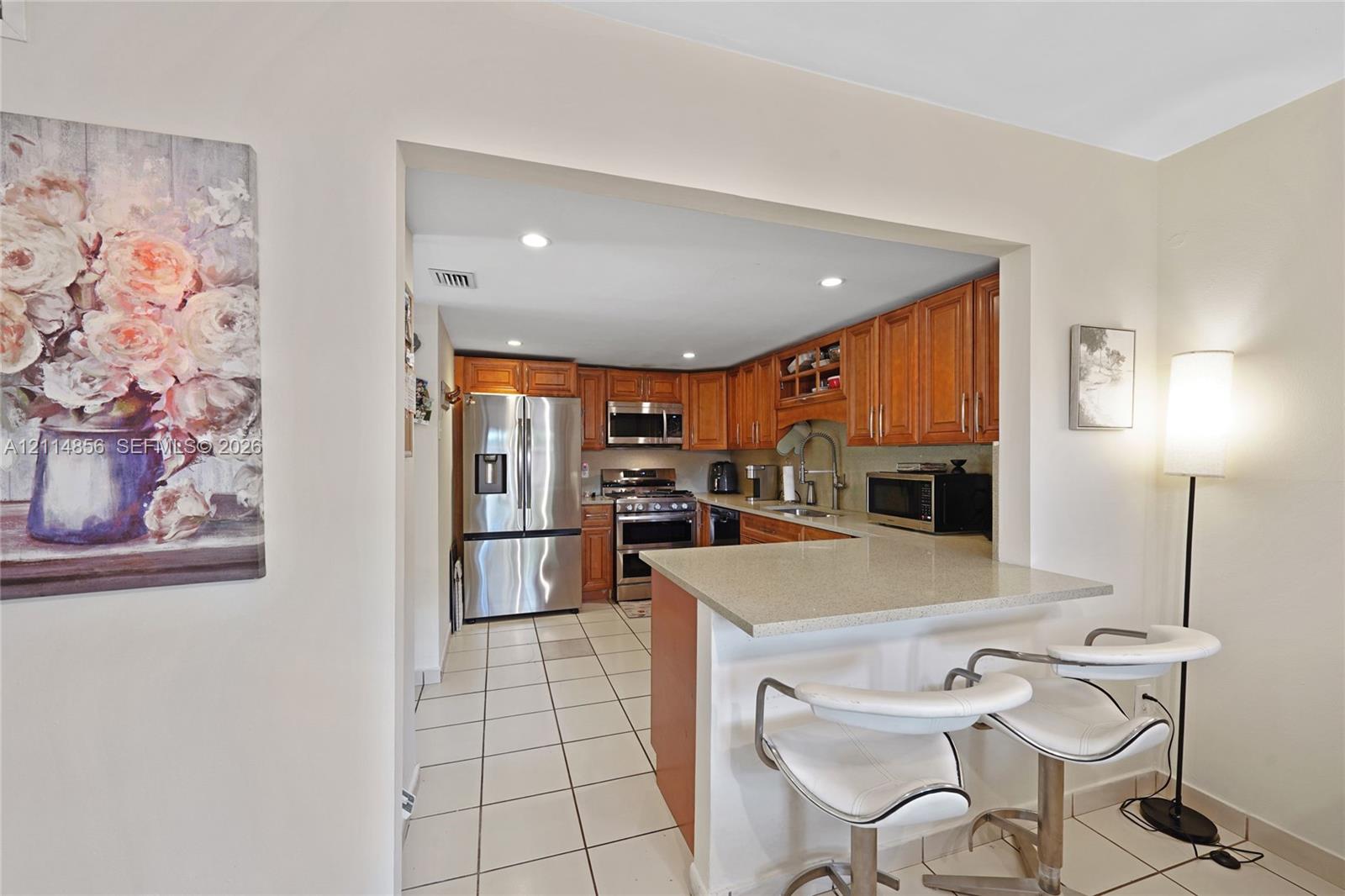 Kitchen featuring wood cabinetry, stainless steel appliances, solid surface countertops, and tiled flooring Kitchen featuring wood cabinetry, stainless steel appliances, solid surface countertops, and tiled flooring