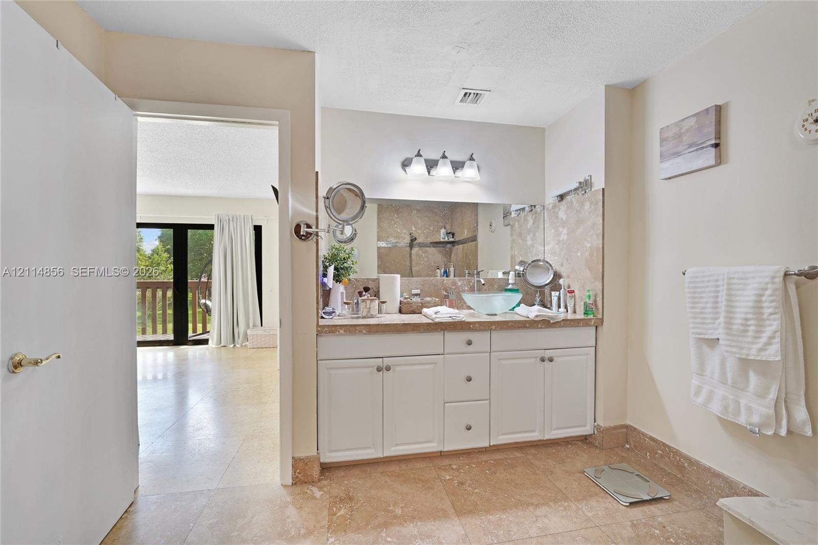 Bathroom featuring a vanity with white cabinetry, a glass vessel sink, stone-finish countertop, full-width mirror, and three-light fixture