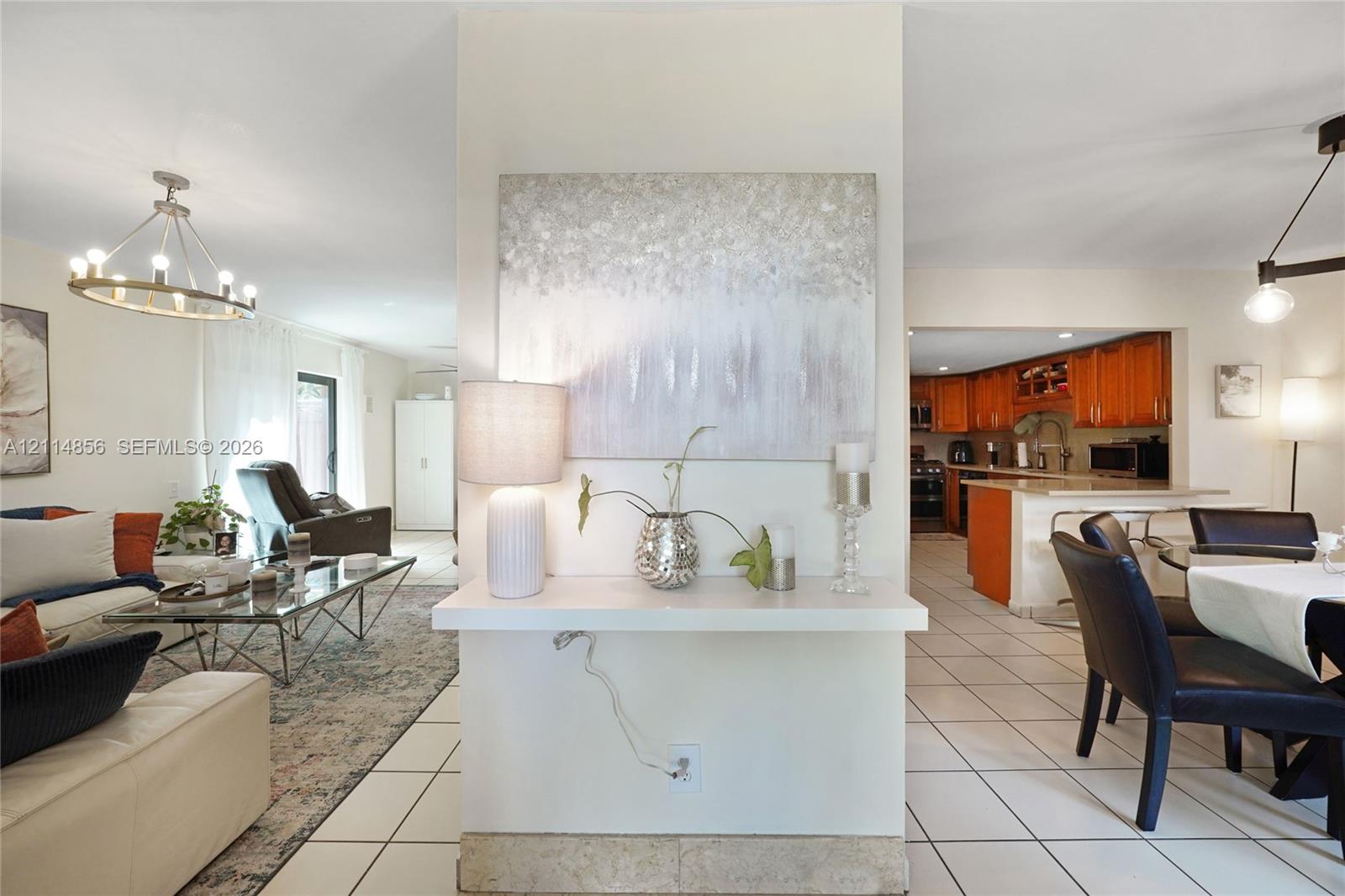 Open-concept interior featuring large-format tile flooring, central partition wall with built-in display shelf, and chandelier lighting Open-concept interior featuring large-format tile flooring, central partition wall with built-in display shelf, and chandelier lighting