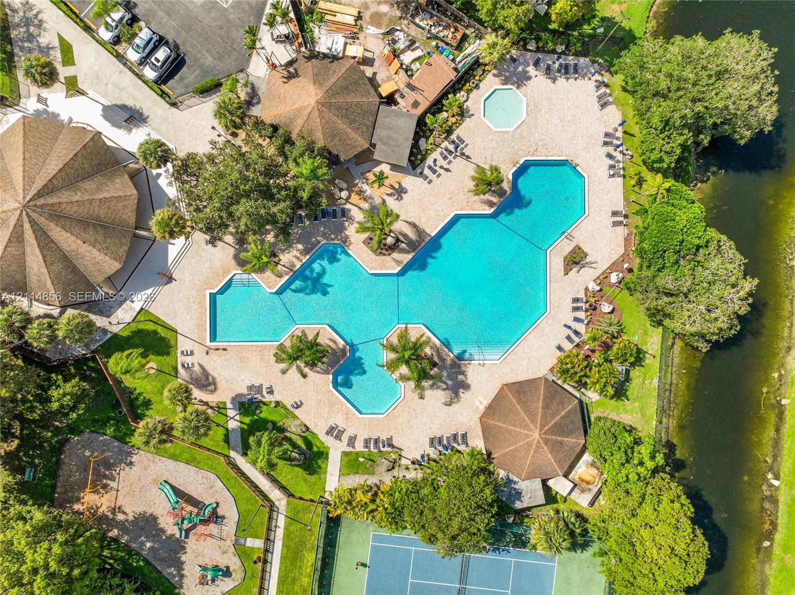 Large-scale community swimming pool, separate spa, hardscaped patio surround, tennis court, and playground area