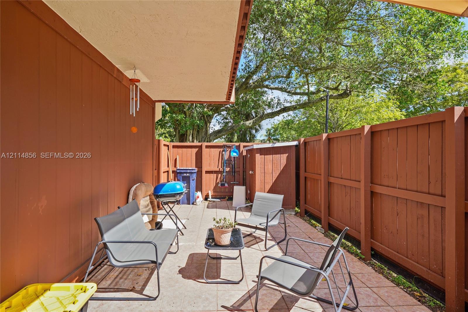 Covered patio featuring ceramic tile flooring, solid wood-panel fencing, and a built-in outdoor storage unit