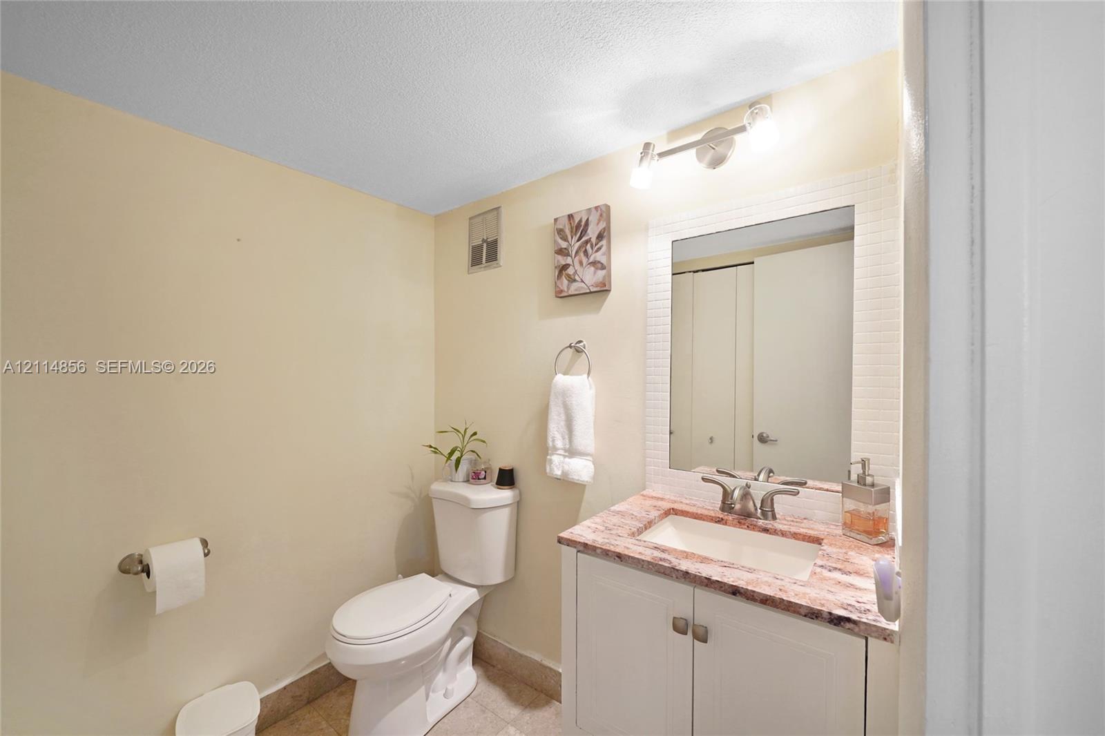 Vanity cabinet featuring stone countertop, integrated sink with dual-handle faucet, wall-mounted mirror, and multi-bulb light fixture