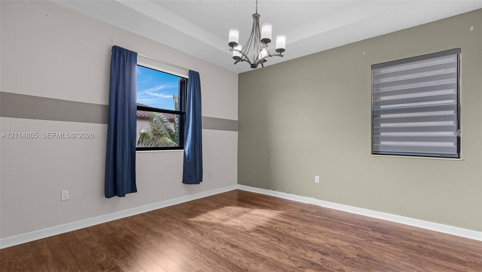 Tray ceiling featuring a multi-arm chandelier, wood-finish flooring, and horizontal window treatments