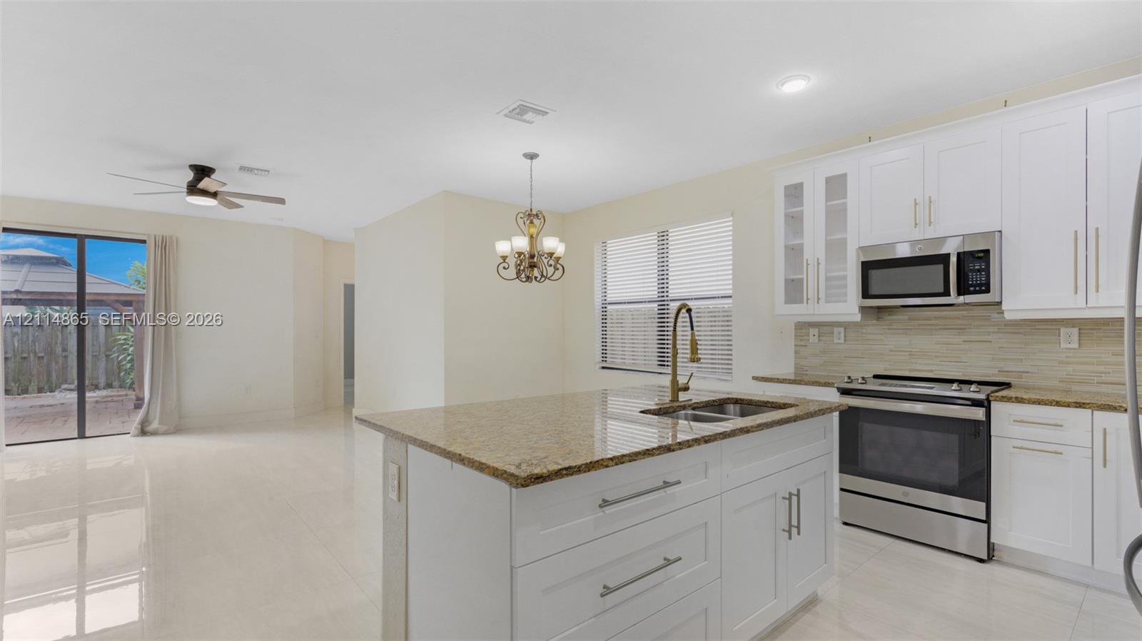 Kitchen featuring white shaker-style cabinetry, stone-surface countertops, stainless steel appliances, a center island with an undermount sink, and tile flooring