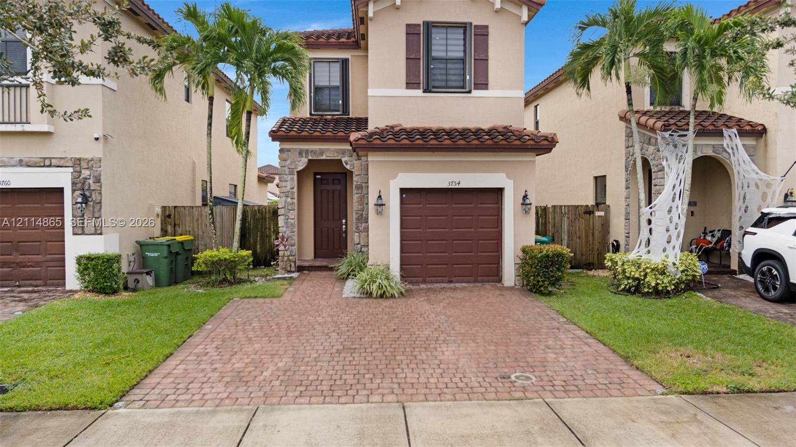 Stucco exterior featuring stone veneer accents, terracotta-style roof tiles, paver driveway, and an arched entryway