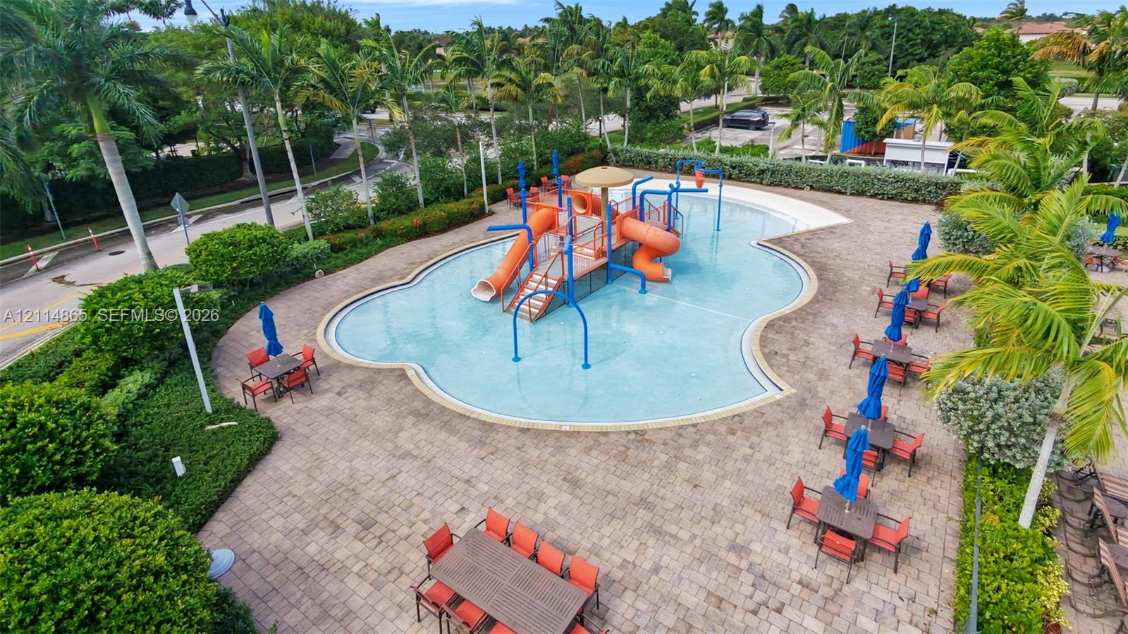 Community pool area featuring a water slide, integrated splash pad, paver patio, and mature palm landscaping