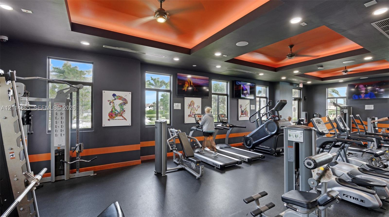 Fitness center featuring recessed tray ceilings with accent lighting, multiple ceiling fans, recessed lighting, and large windows