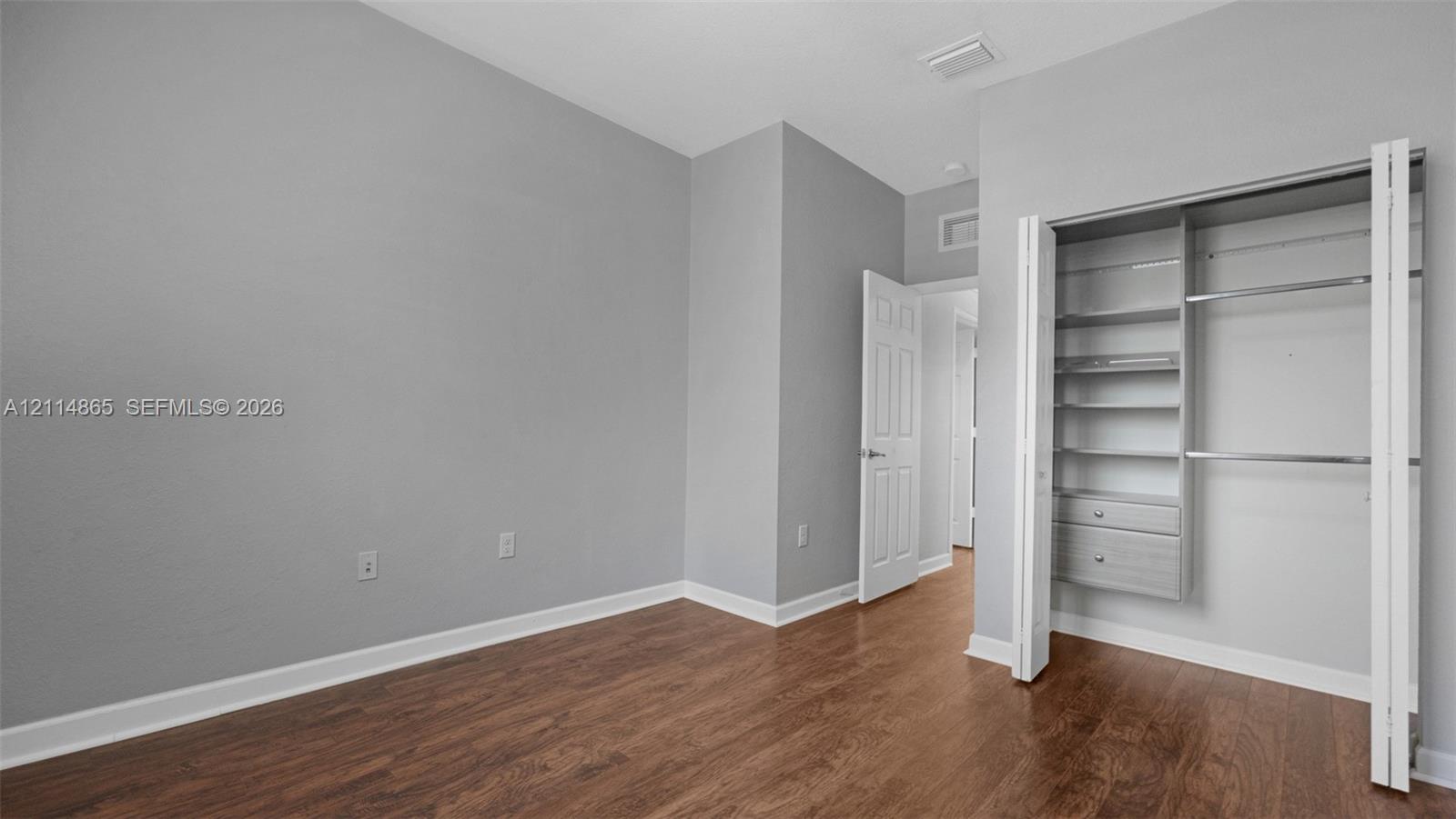 Room featuring wood-finish flooring, neutral wall paint, and a built-in closet system with adjustable shelving and integrated drawers