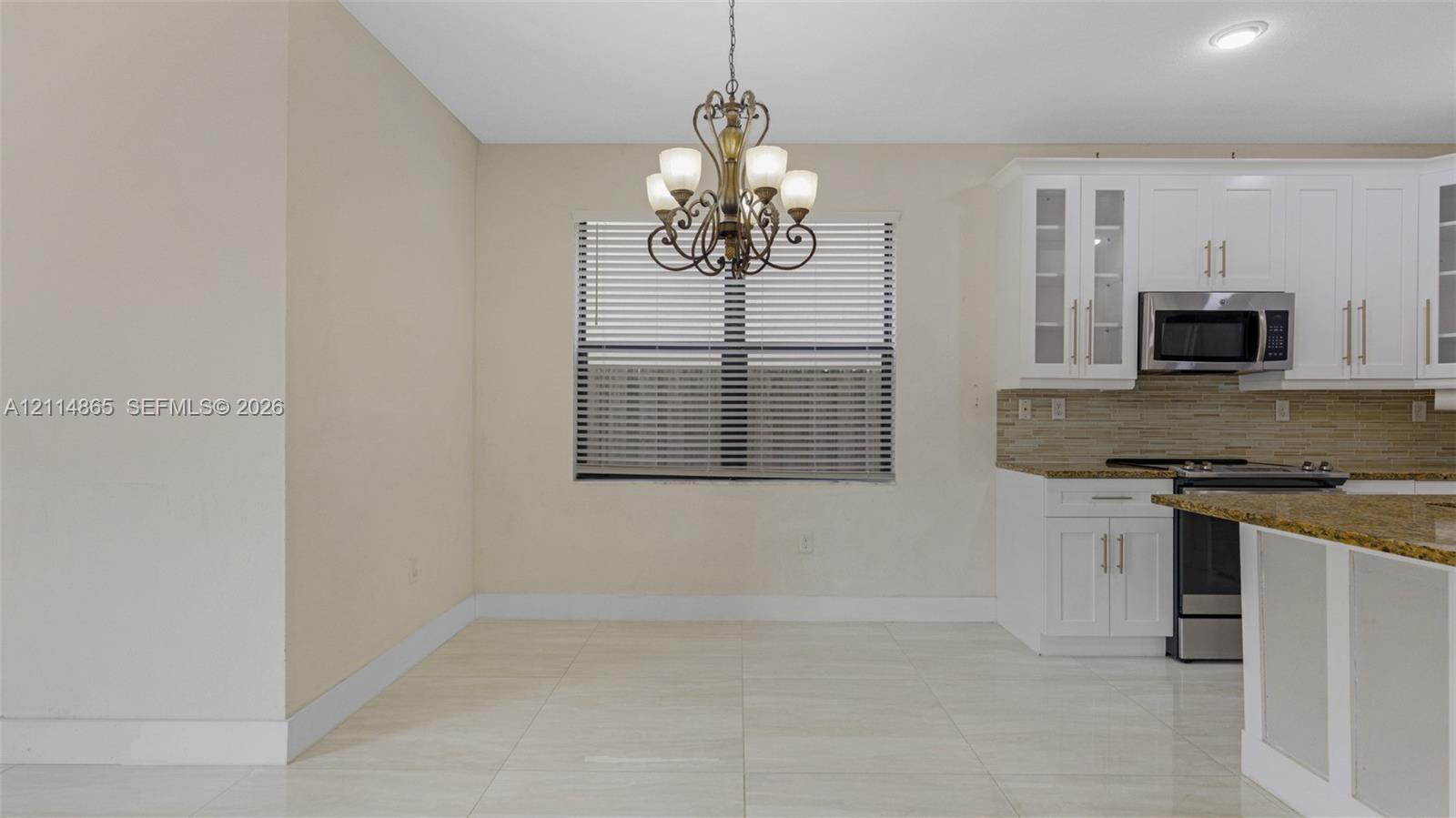 Kitchen featuring white cabinetry with glass-panel accents, stone-finish countertops, stainless steel appliances, tile flooring, and a decorative chandelier