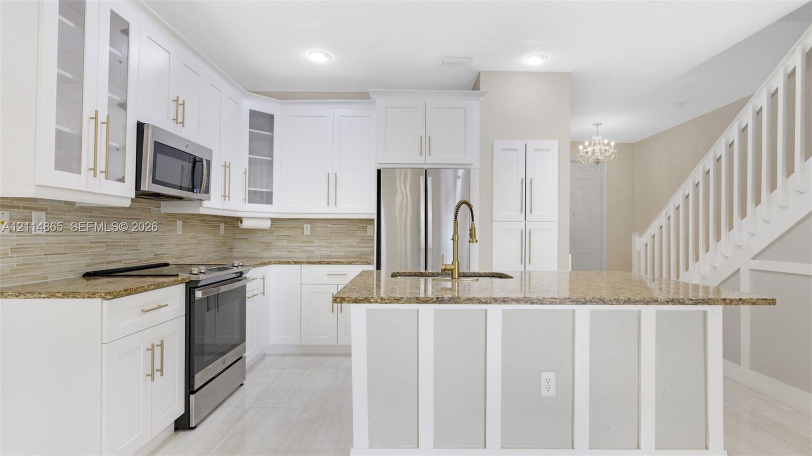 Kitchen featuring white shaker-style cabinetry, a central island with a stone countertop, a linear tile backsplash, stainless steel appliances, and wood-finish flooring