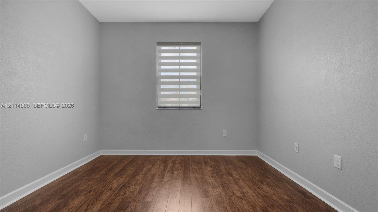 Neutral-toned walls featuring wood-finish flooring and a window fitted with adjustable light-filtering blinds