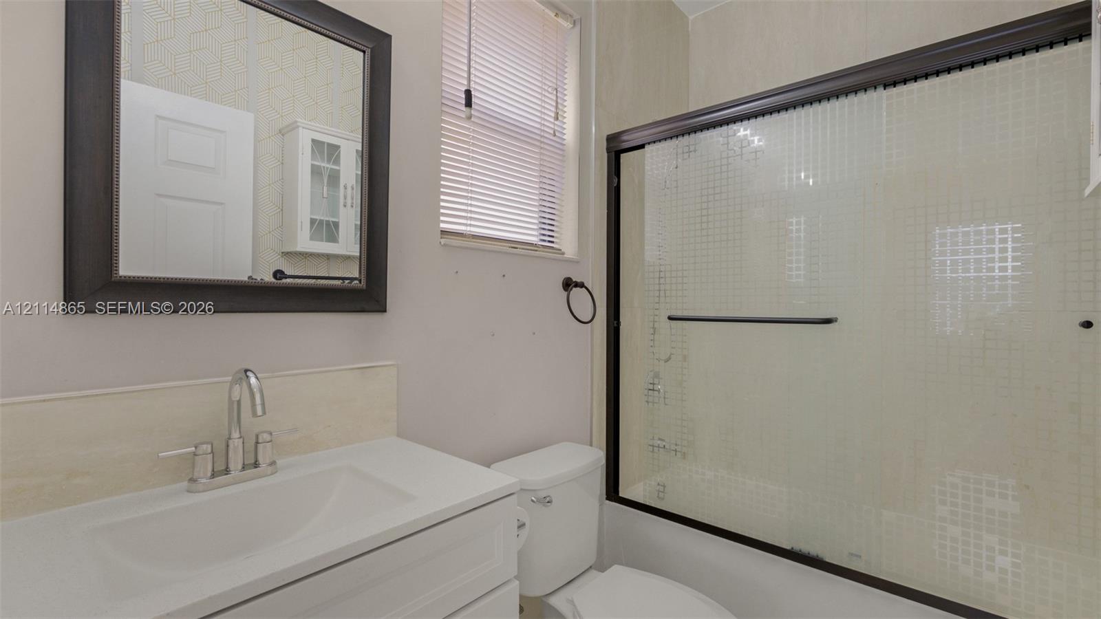 Full guest bath, 1st floor! Bathroom featuring a vanity with a white countertop and integrated sink, a framed wall mirror, a white cabinet, and a bathtub with sliding glass doors and a dark frame